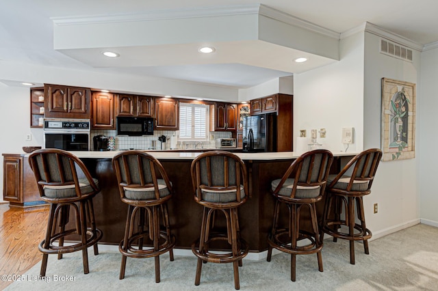 kitchen featuring black appliances, crown molding, kitchen peninsula, a kitchen bar, and tasteful backsplash