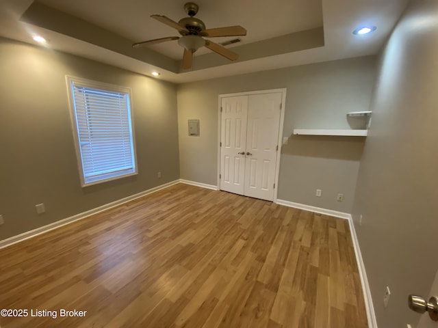 unfurnished room featuring a raised ceiling, electric panel, ceiling fan, and light hardwood / wood-style flooring