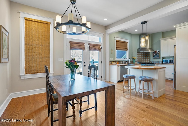 dining space with sink, a chandelier, light hardwood / wood-style floors, beam ceiling, and french doors