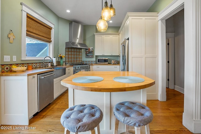 kitchen featuring wall chimney range hood, white cabinets, premium appliances, and decorative light fixtures