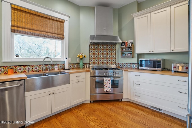 kitchen featuring wall chimney range hood, sink, white cabinetry, stainless steel appliances, and light wood-type flooring