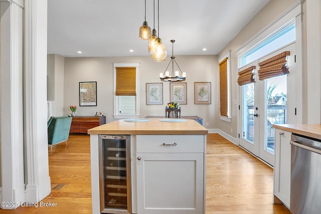 kitchen featuring decorative light fixtures, butcher block counters, white cabinets, beverage cooler, and stainless steel dishwasher