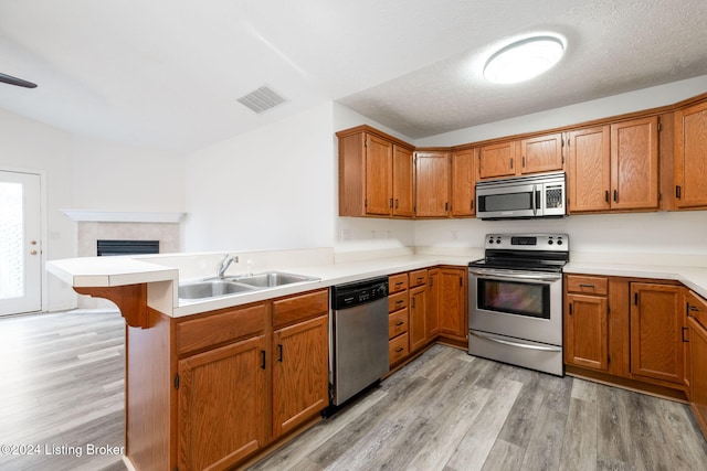 kitchen with sink, stainless steel appliances, light hardwood / wood-style flooring, kitchen peninsula, and a textured ceiling