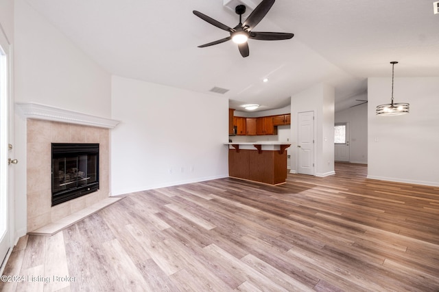 unfurnished living room with light hardwood / wood-style flooring, vaulted ceiling, ceiling fan, and a tiled fireplace