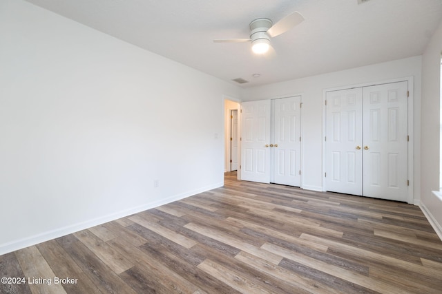 unfurnished bedroom with hardwood / wood-style flooring, ceiling fan, and multiple closets