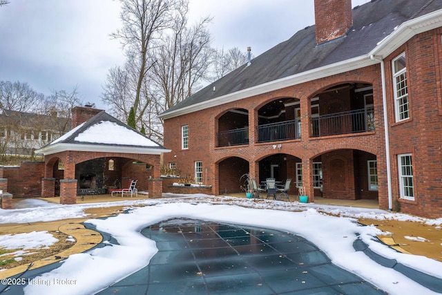 snow covered pool featuring a fireplace and a patio