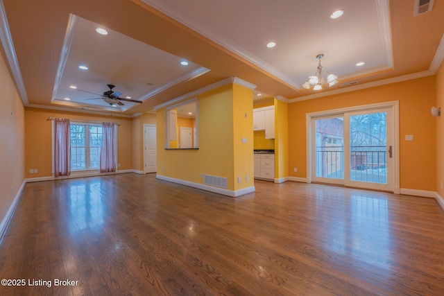 unfurnished living room with ceiling fan with notable chandelier, ornamental molding, a tray ceiling, and hardwood / wood-style floors