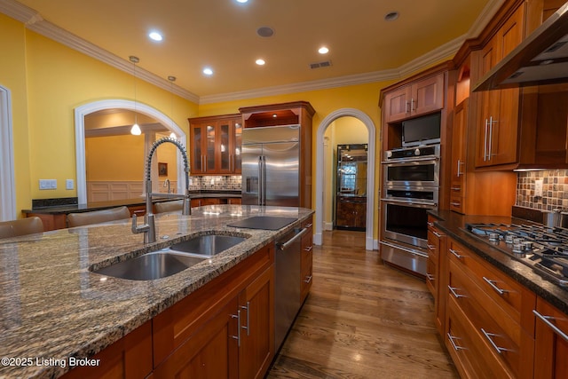 kitchen featuring sink, dark stone counters, wall chimney exhaust hood, and appliances with stainless steel finishes