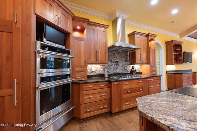 kitchen featuring crown molding, appliances with stainless steel finishes, light hardwood / wood-style floors, decorative backsplash, and wall chimney exhaust hood