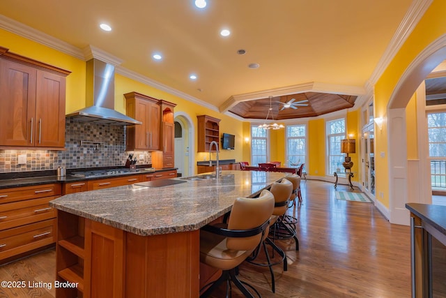 kitchen featuring sink, wall chimney range hood, a breakfast bar, a kitchen island with sink, and backsplash