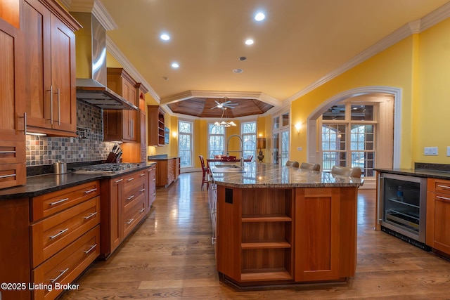 kitchen with a kitchen bar, stainless steel gas cooktop, sink, a center island with sink, and wall chimney range hood