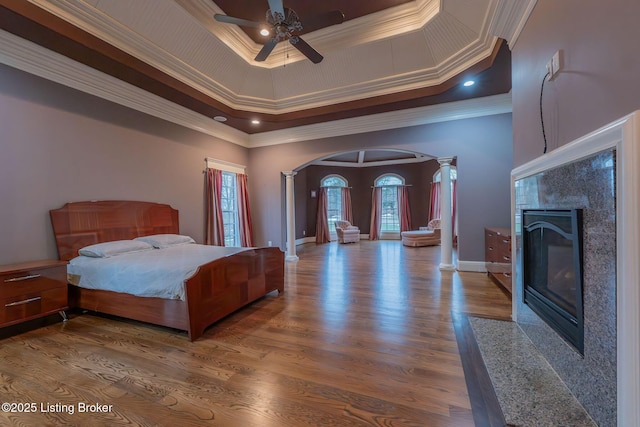 bedroom with a tray ceiling, wood-type flooring, ornamental molding, a high end fireplace, and ornate columns