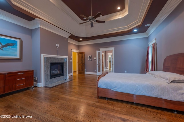 bedroom featuring a tiled fireplace, crown molding, dark hardwood / wood-style floors, and a tray ceiling