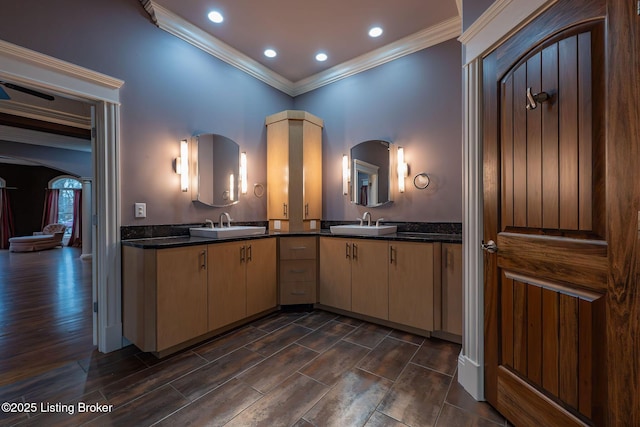 kitchen with light brown cabinetry, sink, crown molding, and dark stone counters