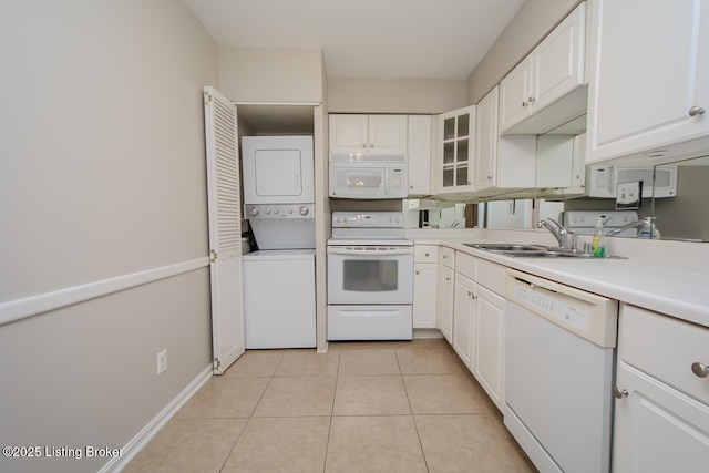 kitchen featuring white appliances, sink, stacked washer and dryer, light tile patterned flooring, and white cabinetry