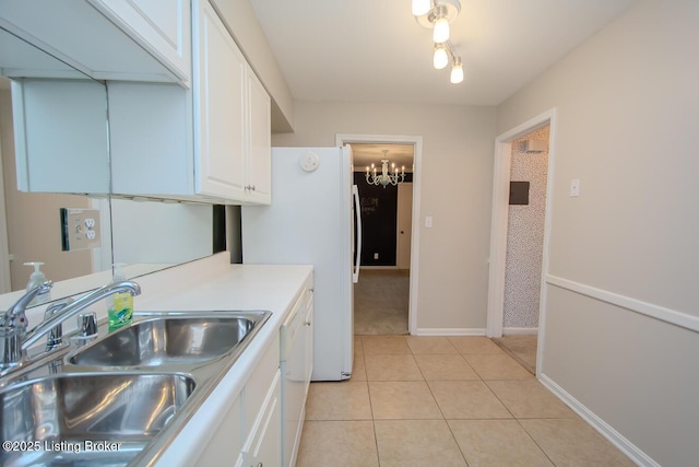 kitchen with white appliances, sink, light tile patterned floors, white cabinetry, and a chandelier