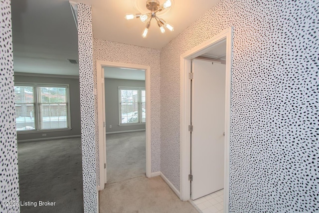 hallway with light carpet and a chandelier