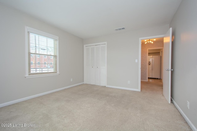 unfurnished bedroom featuring a notable chandelier, white fridge with ice dispenser, light carpet, and a closet