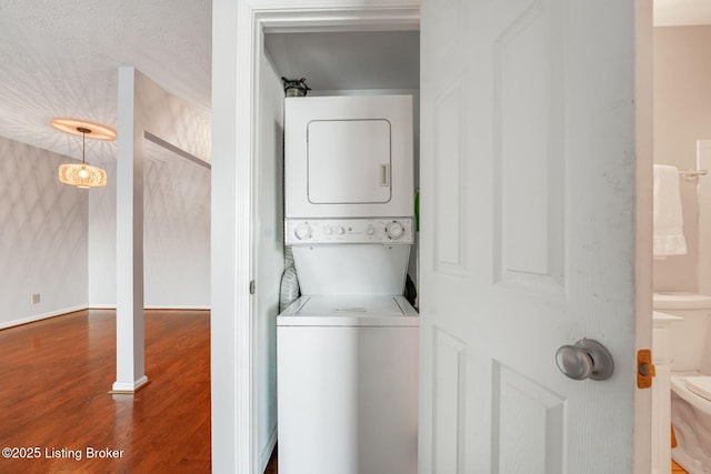 clothes washing area with hardwood / wood-style flooring, stacked washer and dryer, and a textured ceiling