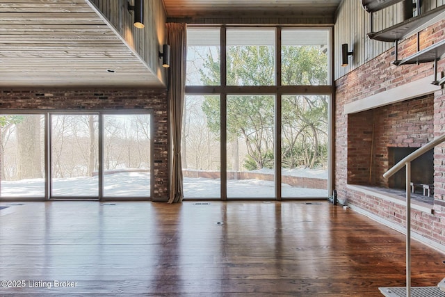 unfurnished living room with hardwood / wood-style flooring, a towering ceiling, and brick wall