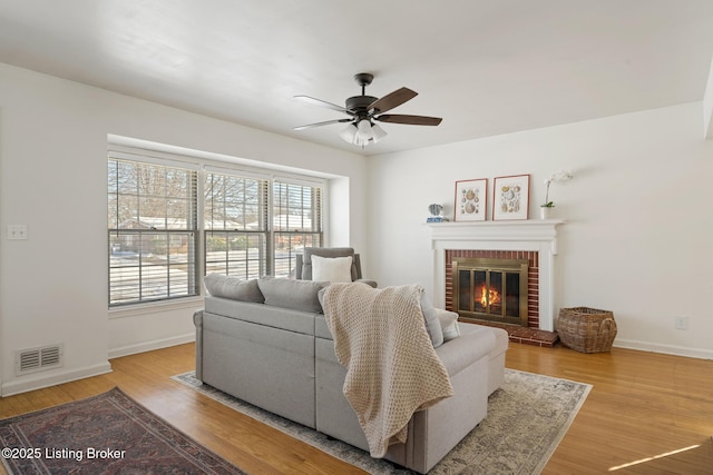 living room featuring ceiling fan, light hardwood / wood-style floors, and a brick fireplace