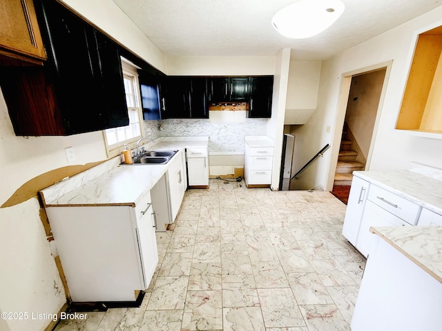 kitchen featuring a sink, marble finish floor, light countertops, dark cabinetry, and tasteful backsplash