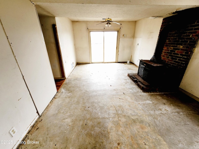 unfurnished living room featuring a wood stove and ceiling fan