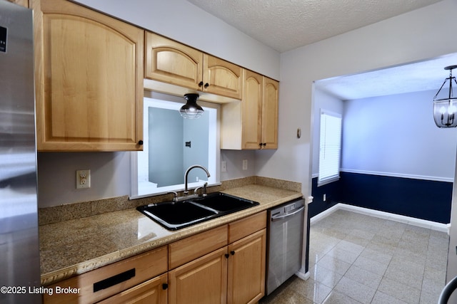 kitchen with a textured ceiling, hanging light fixtures, light brown cabinetry, appliances with stainless steel finishes, and sink