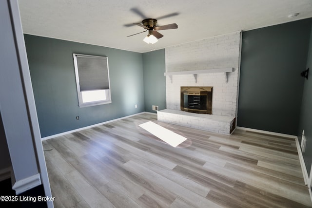 unfurnished living room featuring a brick fireplace, a textured ceiling, ceiling fan, and light hardwood / wood-style flooring