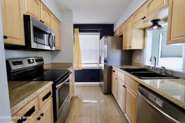 kitchen featuring stainless steel appliances, light brown cabinets, sink, and light stone countertops