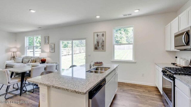 kitchen with light stone countertops, stainless steel appliances, sink, a center island with sink, and white cabinets