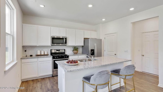 kitchen featuring stainless steel appliances, tasteful backsplash, an island with sink, light hardwood / wood-style floors, and white cabinets