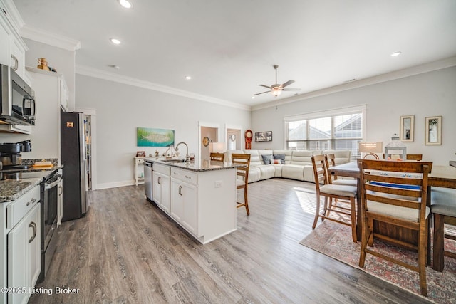 kitchen featuring stainless steel appliances, an island with sink, dark stone countertops, and white cabinetry