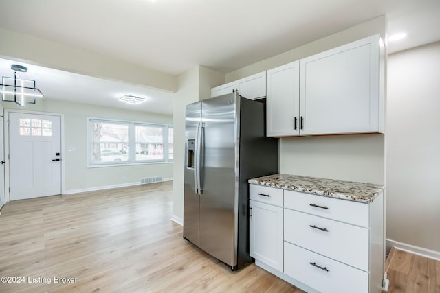 kitchen with light stone counters, white cabinets, stainless steel refrigerator with ice dispenser, and light wood-type flooring