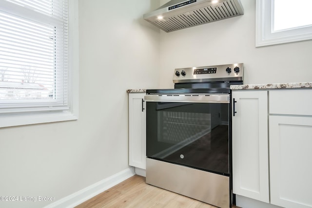 details with light stone counters, wall chimney range hood, electric range, light hardwood / wood-style flooring, and white cabinets