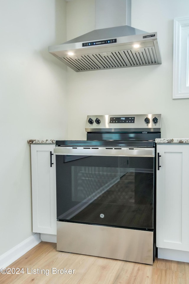 room details with stainless steel range with electric stovetop, white cabinetry, wall chimney range hood, and light hardwood / wood-style floors