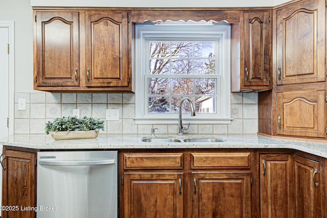 kitchen with stainless steel dishwasher, backsplash, sink, and light stone counters