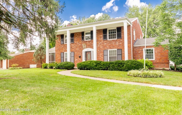 greek revival inspired property featuring brick siding, a chimney, and a front yard