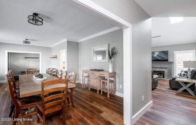 dining room featuring a stone fireplace, dark hardwood / wood-style flooring, a skylight, and ornamental molding