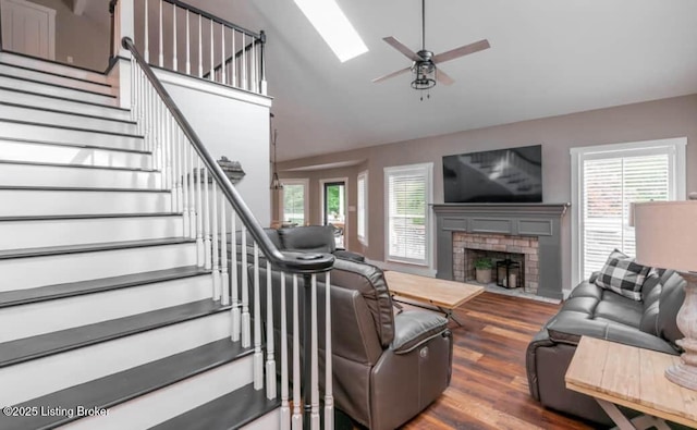 living room with a skylight, ceiling fan, high vaulted ceiling, dark hardwood / wood-style floors, and a fireplace