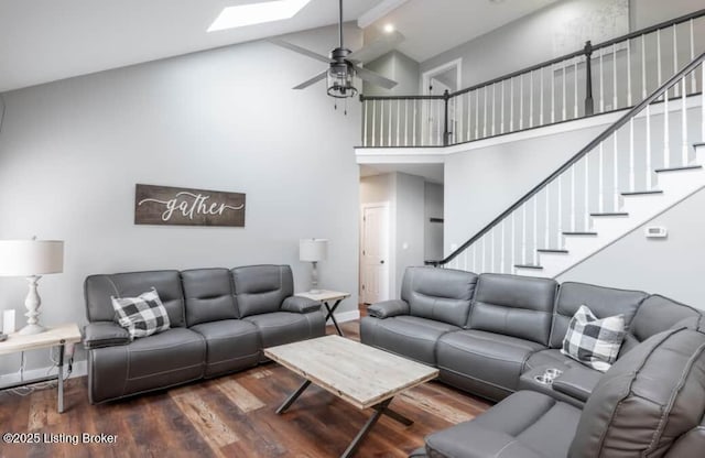 living room featuring dark wood-type flooring, high vaulted ceiling, a skylight, ceiling fan, and beamed ceiling