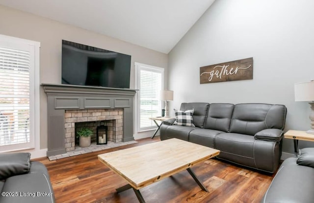 living room with a brick fireplace, hardwood / wood-style flooring, and vaulted ceiling