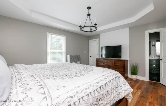 bedroom featuring dark hardwood / wood-style flooring, ensuite bathroom, and a raised ceiling