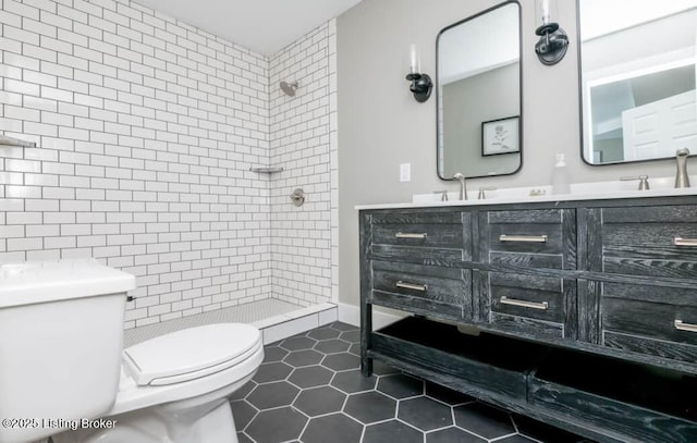 bathroom featuring vanity, tile patterned flooring, toilet, tile walls, and a tile shower