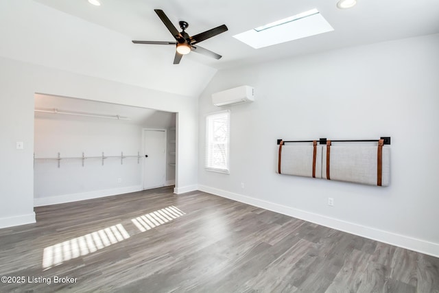 unfurnished living room featuring an AC wall unit, hardwood / wood-style flooring, ceiling fan, and vaulted ceiling with skylight