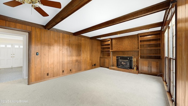 unfurnished living room with a fireplace, wood walls, light colored carpet, beam ceiling, and built in shelves