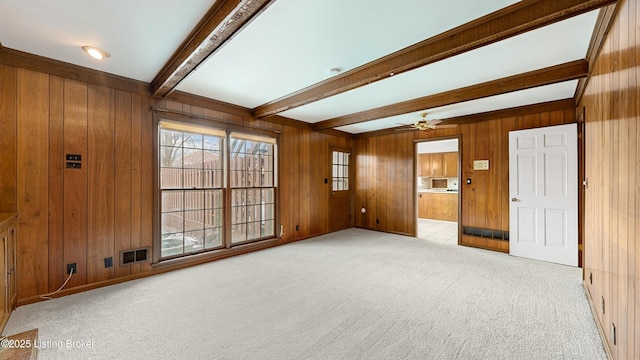 carpeted spare room with ceiling fan, wooden walls, and beam ceiling