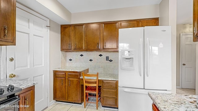 kitchen featuring tasteful backsplash, light stone counters, built in desk, light tile patterned floors, and white refrigerator with ice dispenser