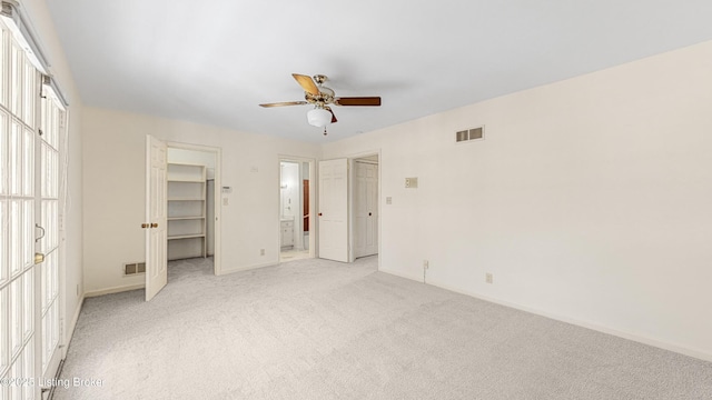 unfurnished bedroom with ceiling fan, a walk in closet, a closet, and light carpet