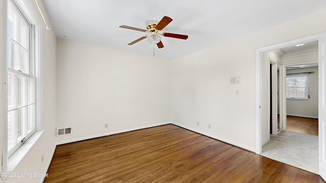 empty room with ceiling fan, crown molding, dark wood-type flooring, and a healthy amount of sunlight